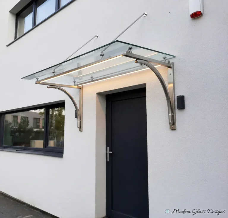 Glass canopy on curved stainless steel brackets with lighting above a dark entry door