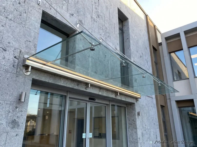 Long glass canopy with a lit stainless wall rail above a building entrance