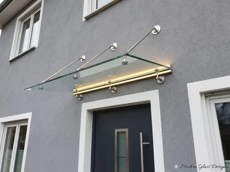 Frameless glass canopy with a lit wall rail and three steel rods above a dark front door