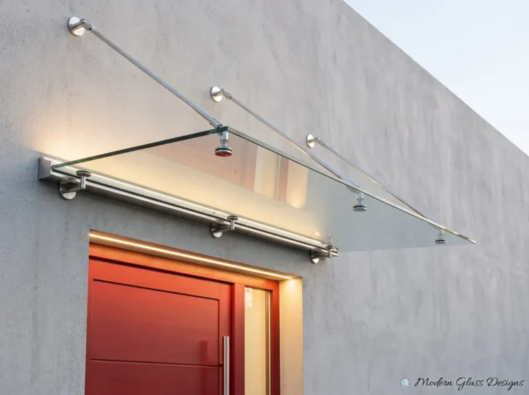 Frameless glass canopy with a lit wall rail and three steel rods above a red front door