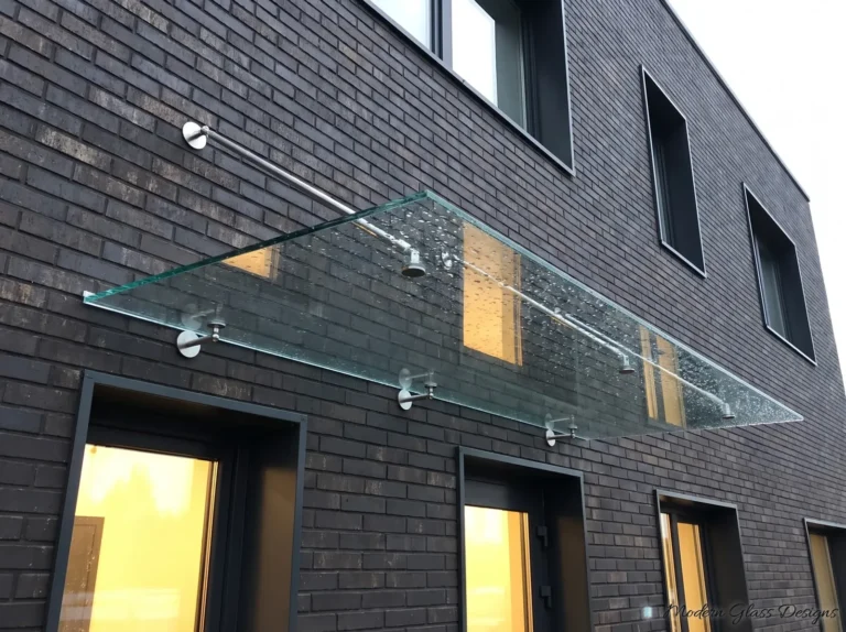 Long frameless glass canopy on steel rods over entry doors on a dark brick wall
