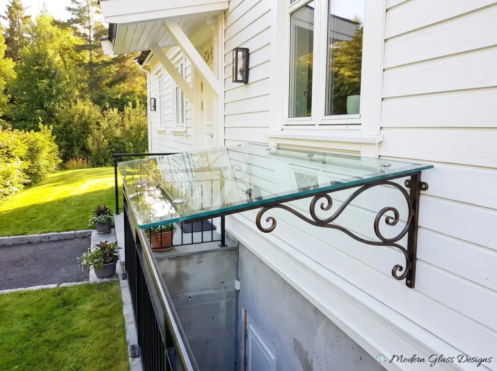Clear glass canopy on bronze scroll brackets above a basement entry