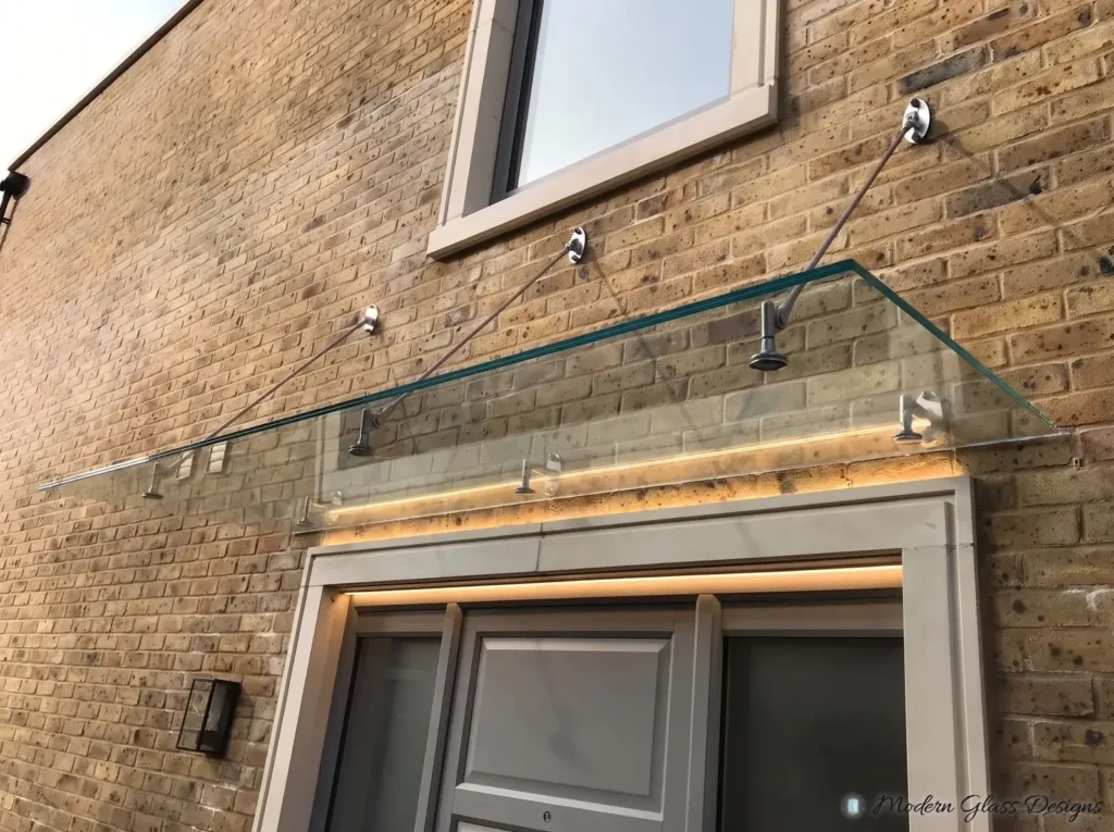 Clear glass canopy on three support rods above a front door on a brick wall