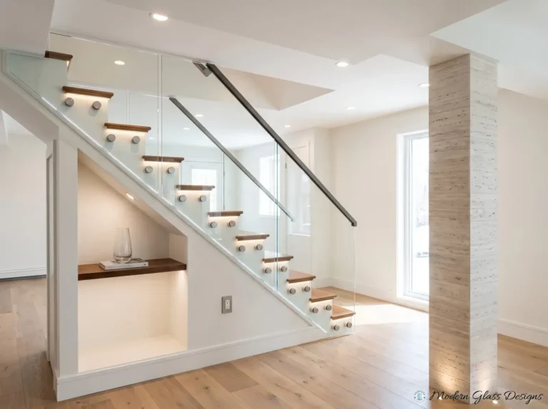 Glass stair railing fixed with standoffs, with a dark handrail and lighted treads