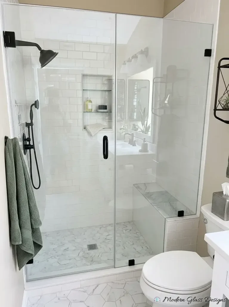 Frameless inline shower door and panel with matte black clamps beside a bench