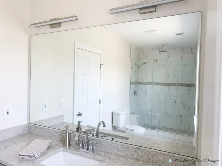 Large frameless vanity mirror reflecting a glass shower