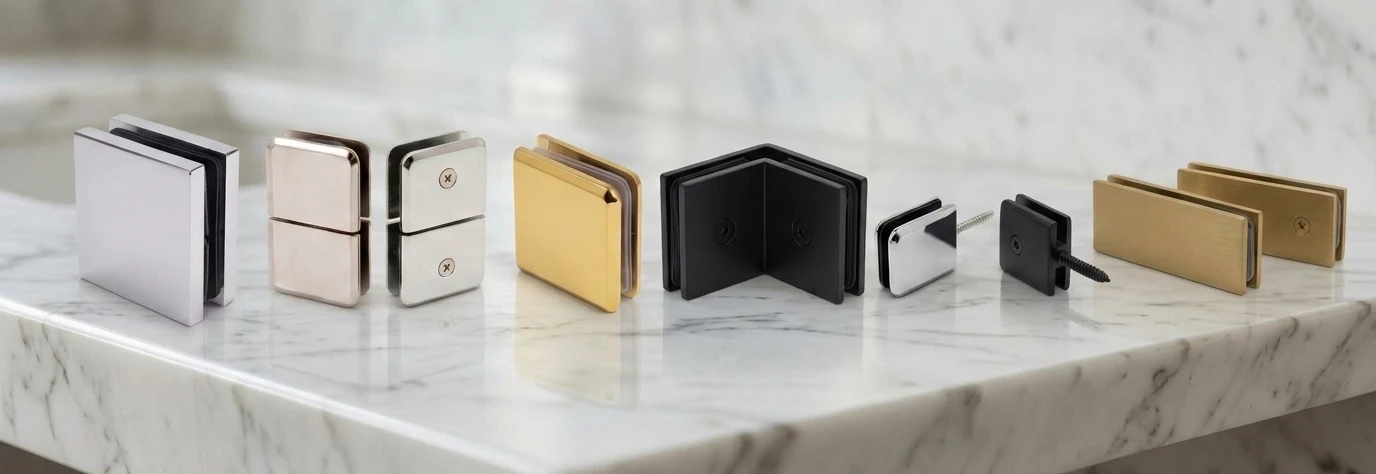Shower glass clamps in chrome, polished nickel, polished brass, matte black and satin brass finishes on a marble counter
