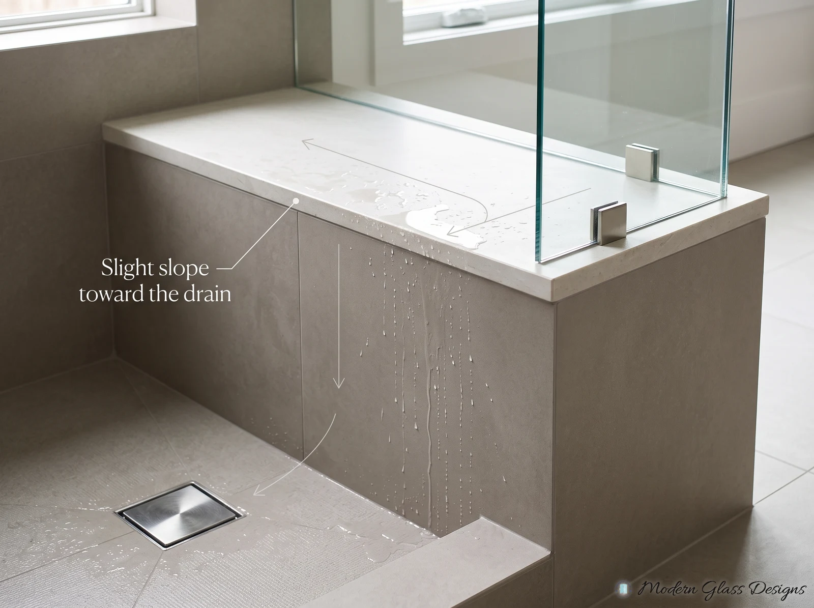 Solid-surface shower bench top under frameless glass, sloped slightly so water runs back toward the drain