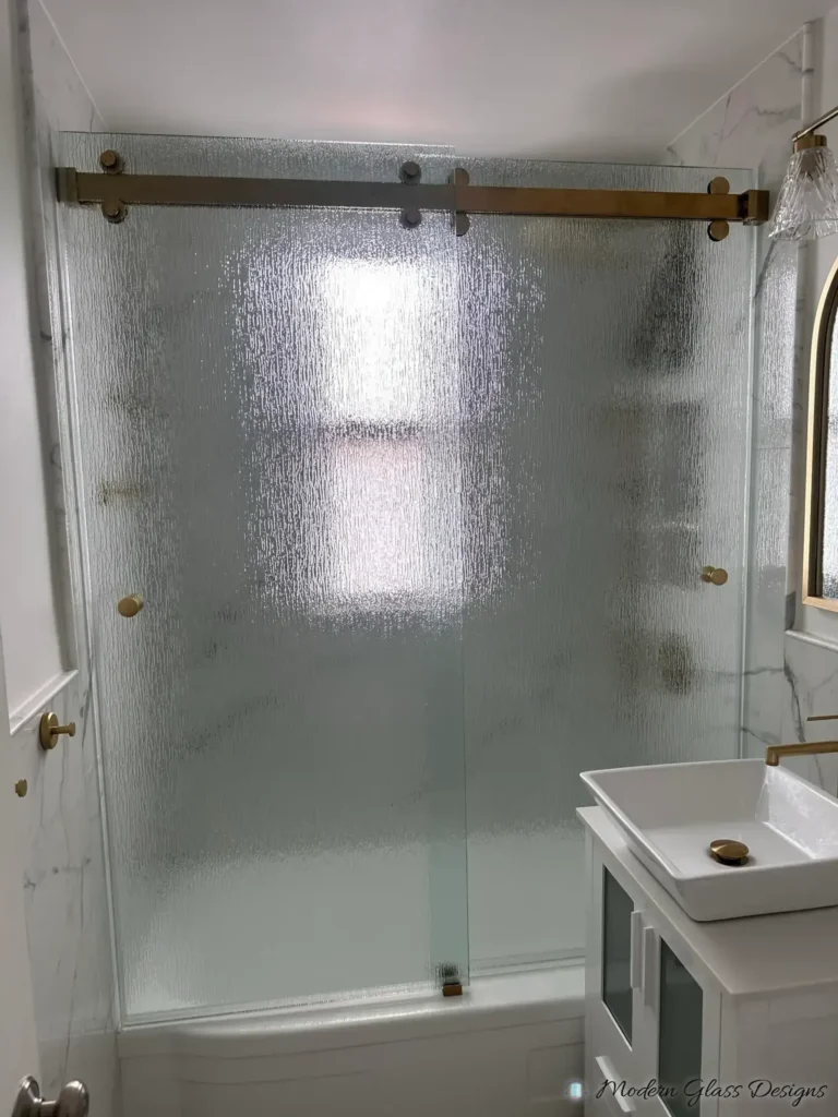 Sliding glass tub door with textured glass and a gold-tone rail